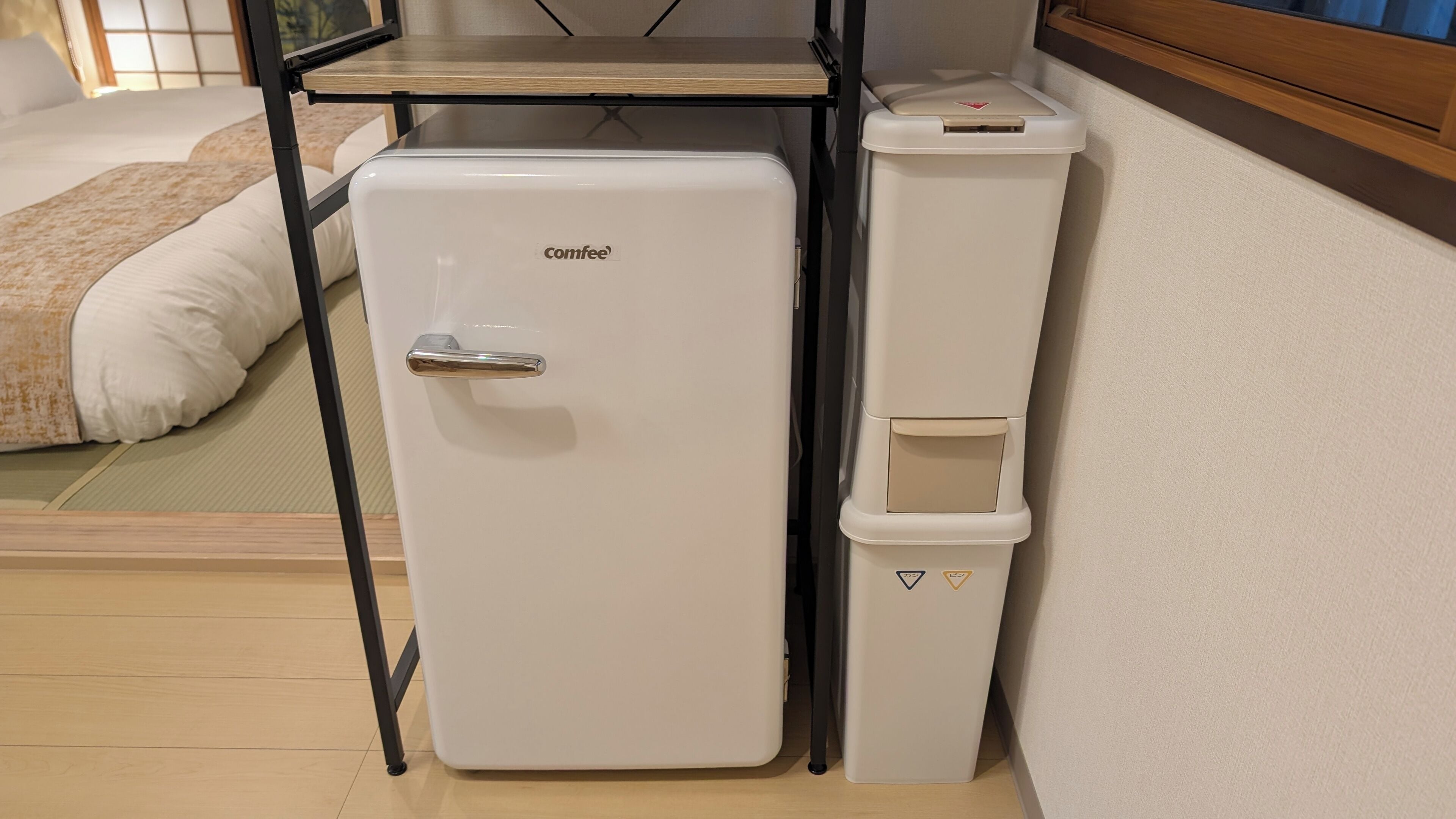 A compact kitchenette with a white refrigerator, a sink, and a trash bin.