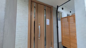 A wooden door with a handle and a window, a white brick wall, and a wooden slatted fence. - Dream Stays SORA (Izumisano)