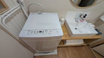 A compact bathroom with a white washing machine, a sink, and a mirror.