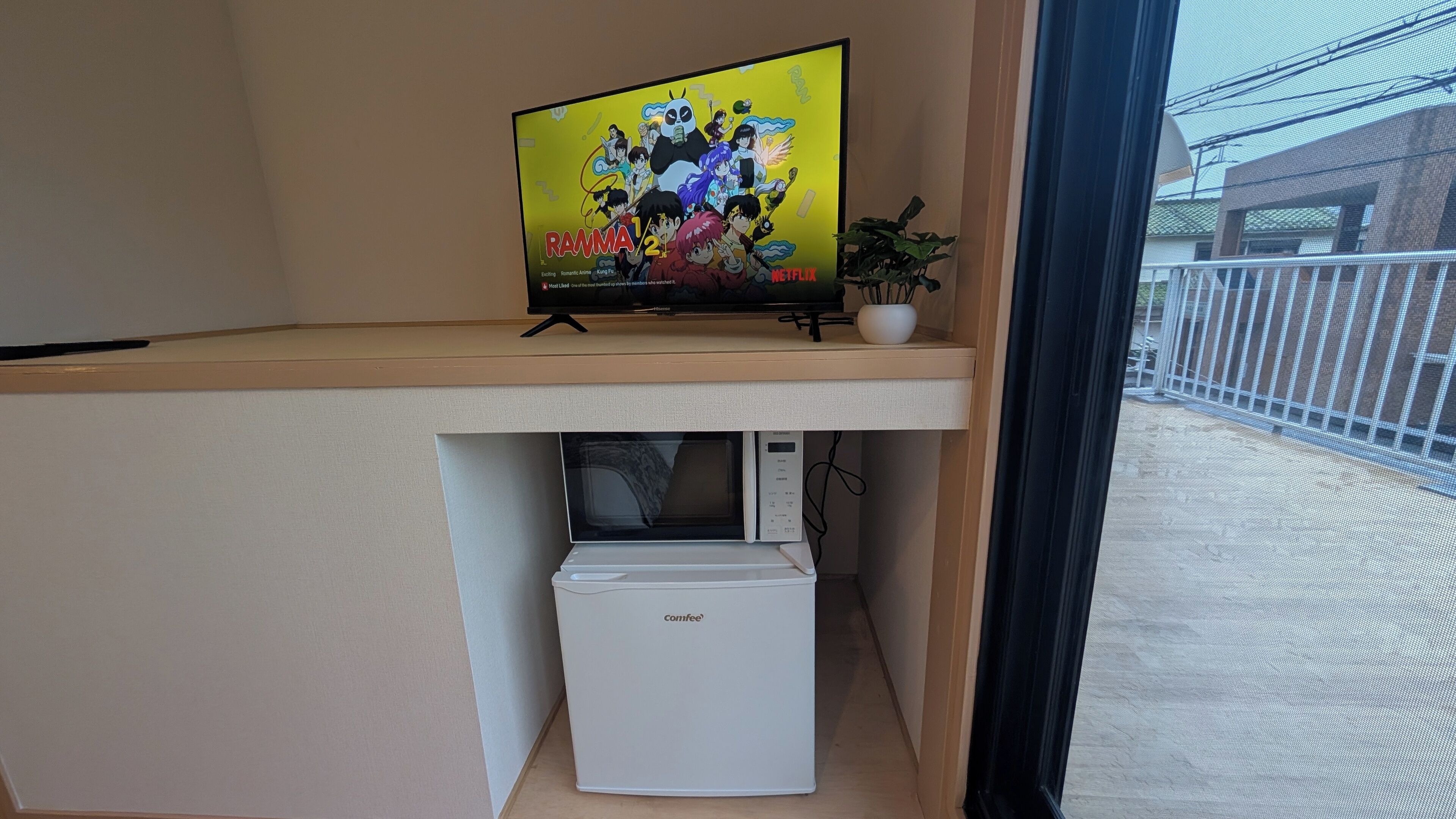 Un téléviseur posé sur une étagère, avec un groupe de personnages d’animation à l’écran, une petite plante en pot et un four à micro-ondes en dessous.