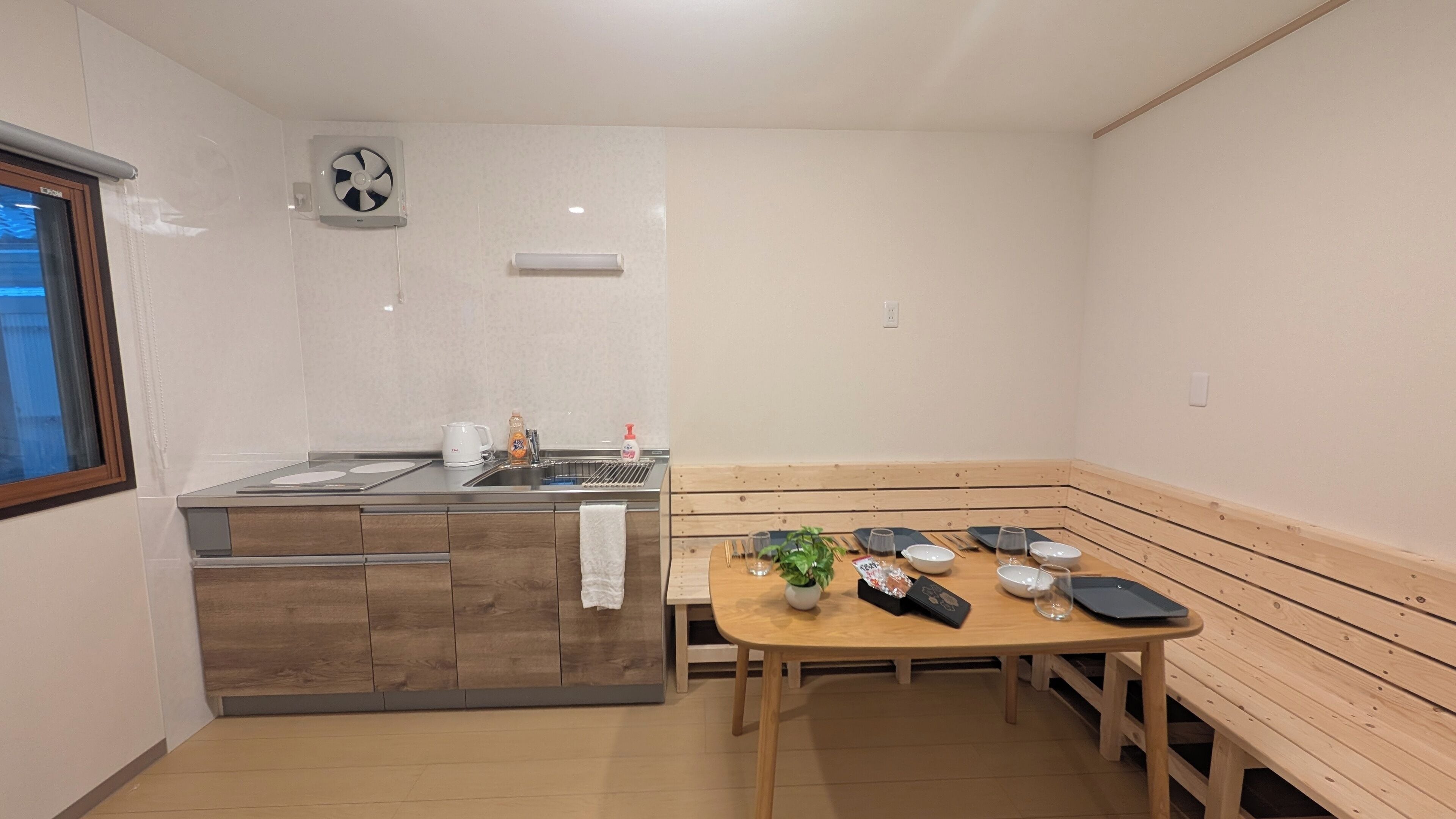 Une cuisine compacte équipée d’une cuisinière intégrée, d’un évier et d’un petit coin repas avec un banc et une table en bois.