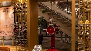 Una bodega con múltiples estantes llenos de botellas de vino, una bomba de vino tinto y una escalera al fondo.