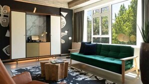 Una sala de estar moderna con un sofá verde, una mesa de centro de madera y un ventanal con vistas a árboles.