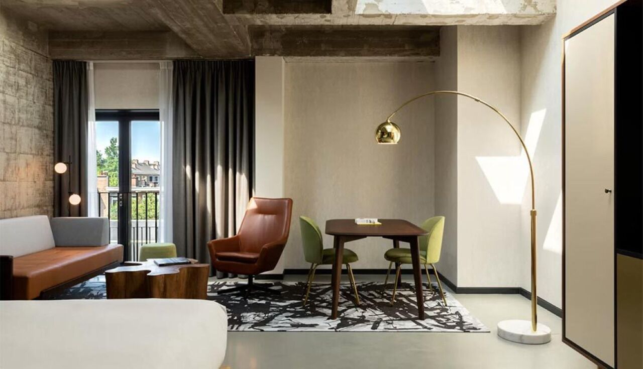 Une chambre d’hôtel moderne, dotée d’un canapé, d’une table à manger avec des chaises, d’une lampe sur pied et offrant une vue sur l’extérieur.