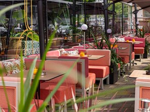 Un espace extérieur aménagé avec des chaises et des tables à coussins rouges, entouré de plantes en pot et de parasols.