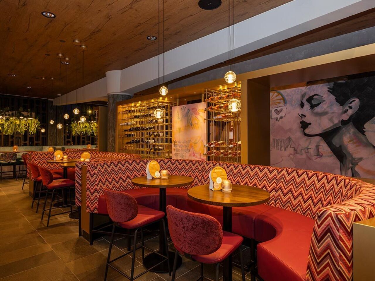 A restaurant with red upholstered booths, round tables, and hanging pendant lights.