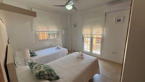 Quarto com duas camas, ventoinha no teto e janelas com grades.