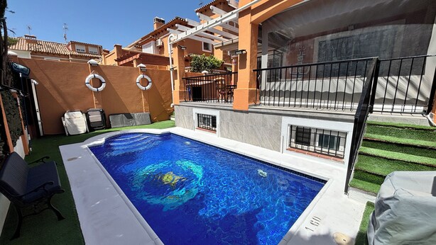 Piscina com superfície de água azul cristalina, rodeada por um terraço com gramado verde e borda de piscina branca.