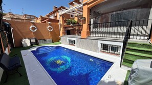 A swimming pool with a clear blue water surface, surrounded by a patio area with a green lawn and a white pool edge.