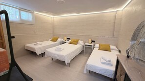 A hotel room with three single beds, each with a white bedspread and a yellow pillow. There is a wooden nightstand with a lamp and a telephone on each side of the beds. The room has a large window with a view of trees, and a ceiling fan is visible on the right side. - "Villa Ana" Semi-detached House in Playamar-Los Alamos Torremolinos with S/Pool (Torremolinos)