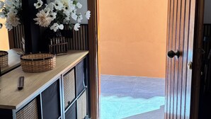 Um corredor com uma porta de madeira que dá para uma área externa, um espelho, um quadro emoldurado e uma cesta em uma bancada.