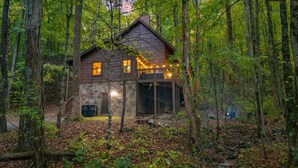 A cabin surrounded by trees with a stone foundation and a wooden deck. - Finding Bigfoot 2 Bedroom Cabin (Sevierville)