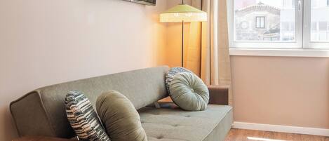 A modern living room with a sofa, a flat-screen TV, a lamp, and a window with curtains.