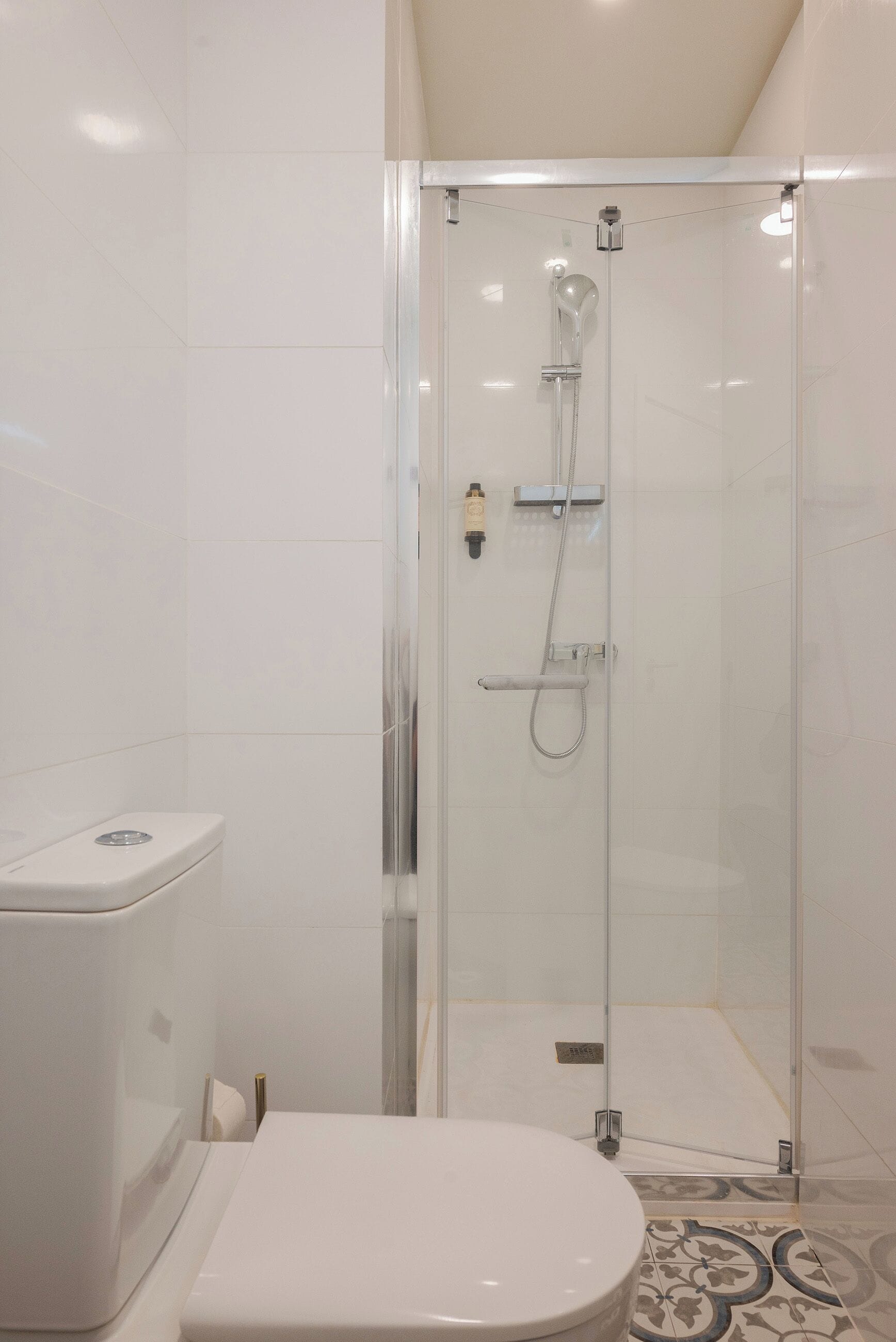A modern bathroom with a glass-enclosed shower, a white toilet, and patterned floor tiles.