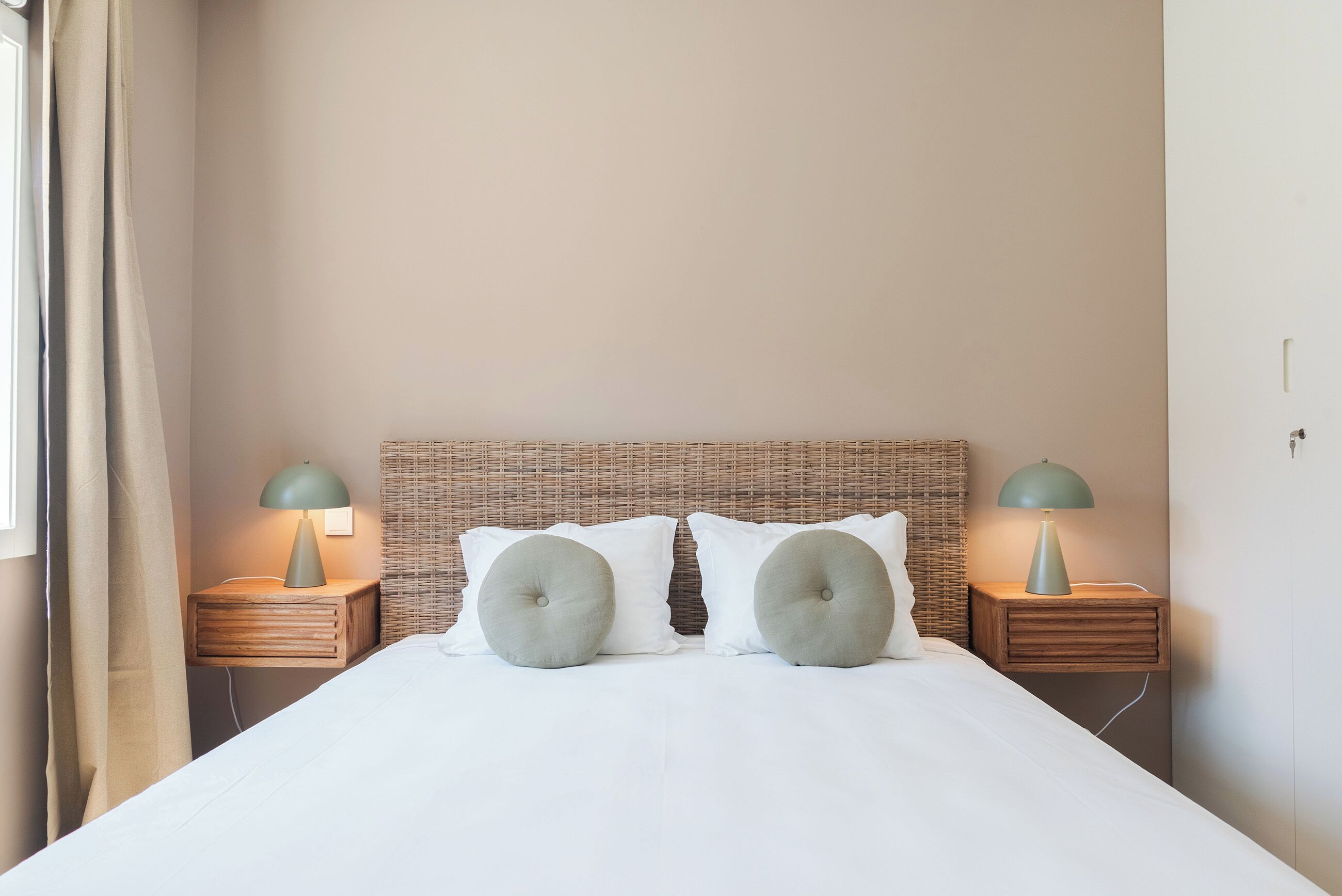 A neatly made bed with two pillows, a wicker headboard, and two bedside tables with lamps.