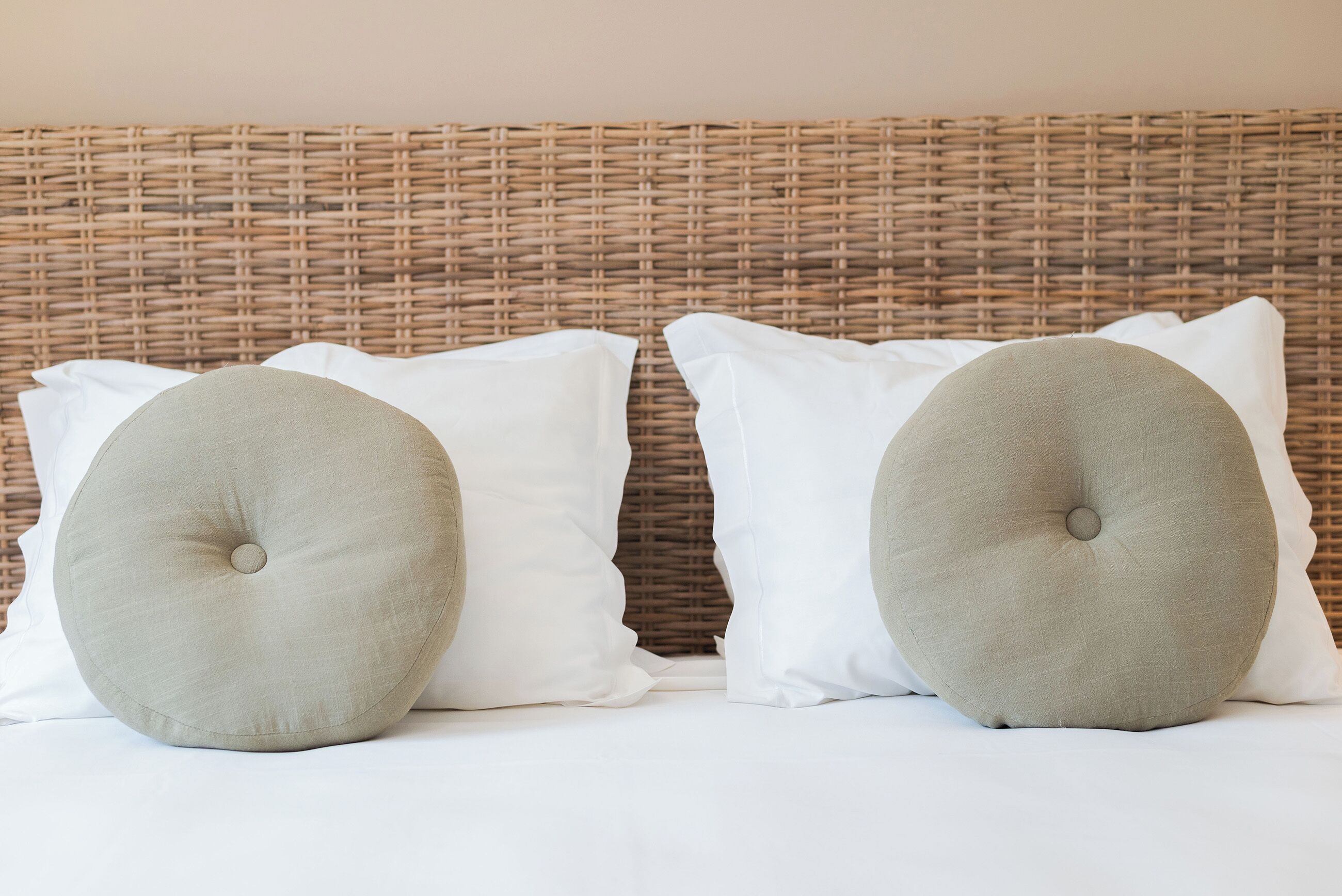 Uma cama com duas almofadas brancas e dois grandes almofuses redondos.