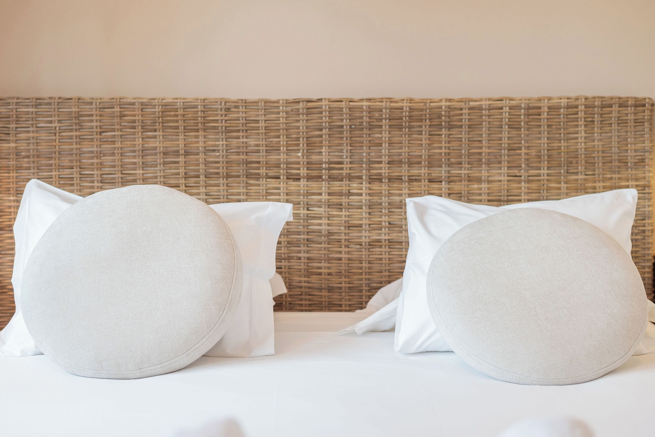 Una cama con dos almohadillas redondas y un cabecero tejido.