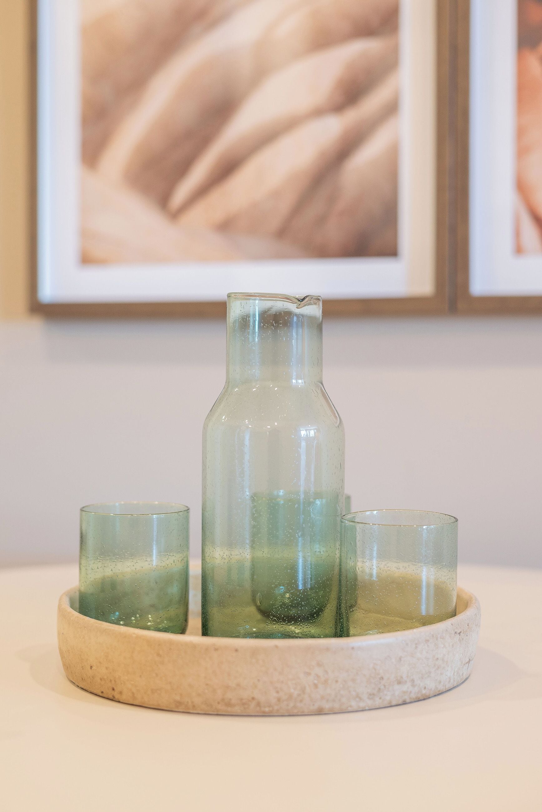 Une bouteille en verre transparent et deux verres posés sur un plateau en céramique rond.