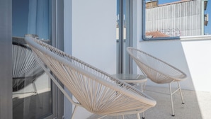 Due poltrone in vimini su un balcone con una porta vetrata e una finestra, e una ringhiera in metallo.