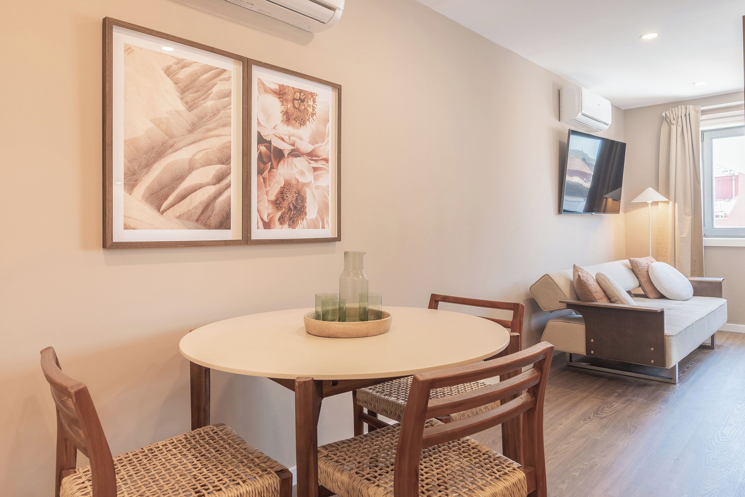 Ein Zimmer mit einem runden Esstisch, Korbstühlen, einer Couch und zwei gerahmten Blumenbildern an der Wand.
