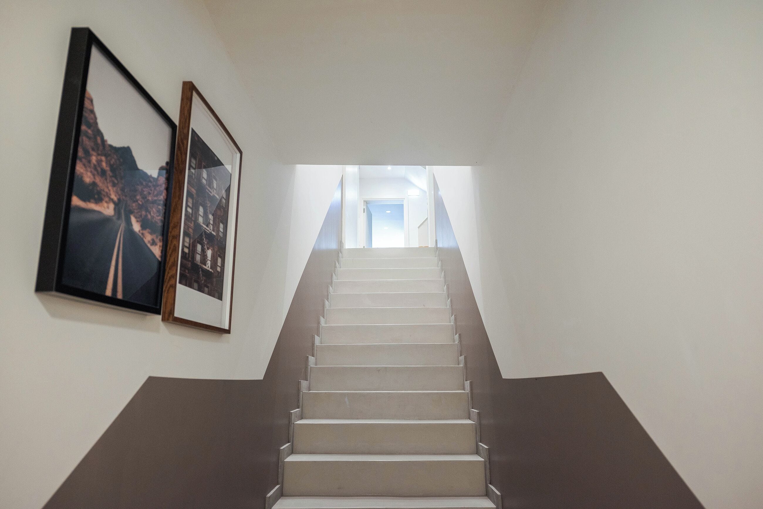 A staircase leading to an upper floor with two framed photographs on the wall.