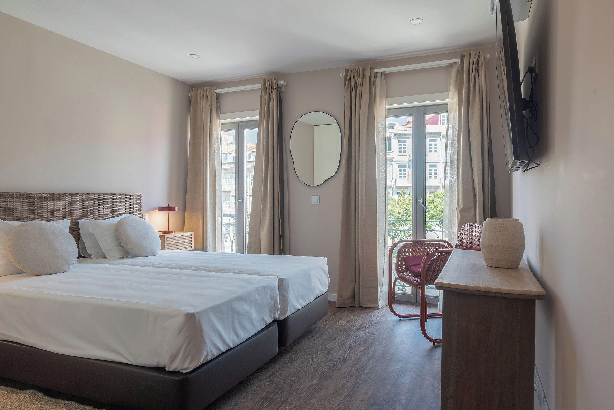 A modern hotel room with a large bed, a flat-screen TV mounted on the wall, a small table, and a chair.
