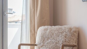 Una poltrona soffice con gambe in legno in una stanza con pavimento in legno e un'ampia finestra con tende.