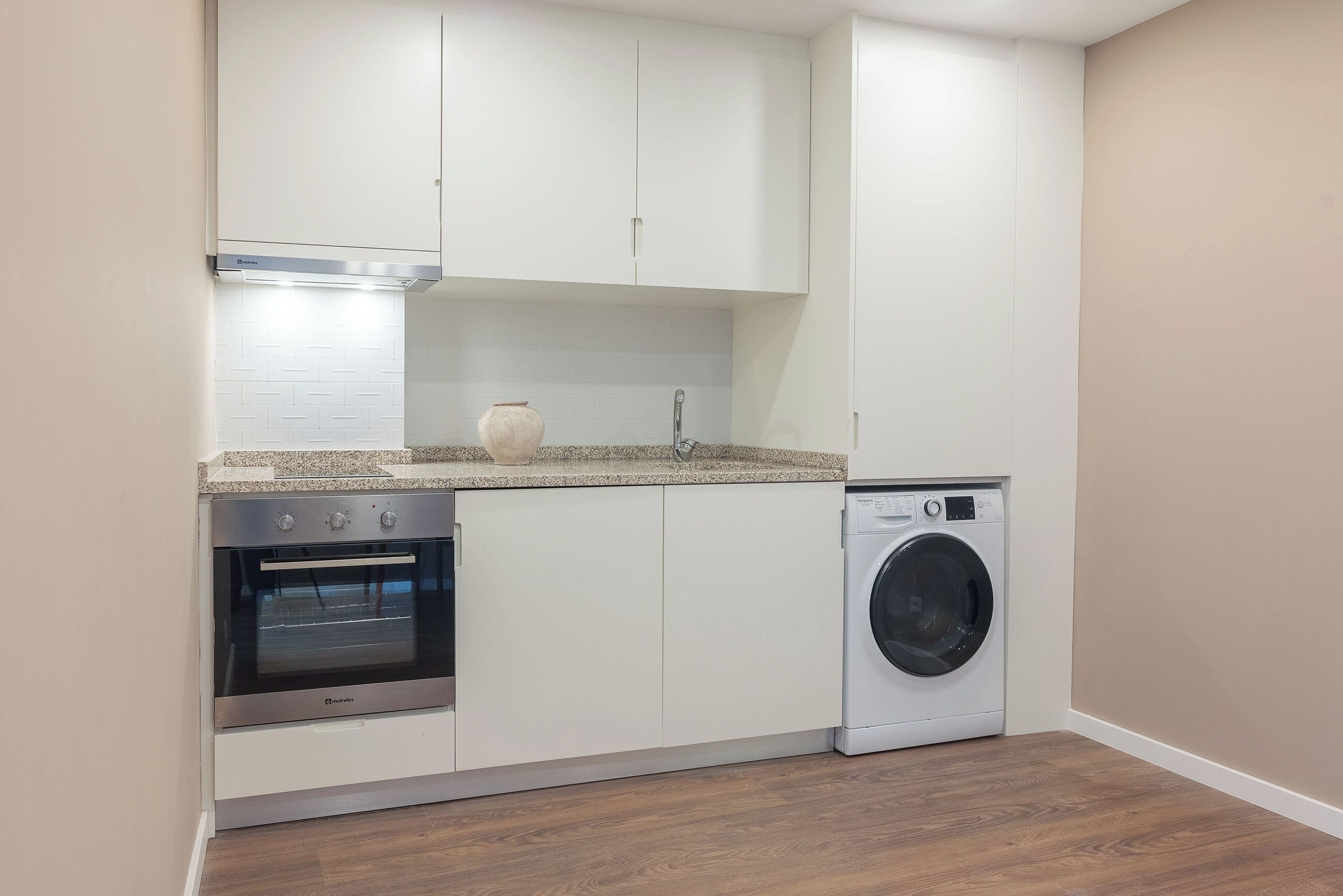 A kitchen with white cabinets, a stainless steel oven, a washing machine, and a tiled backsplash.