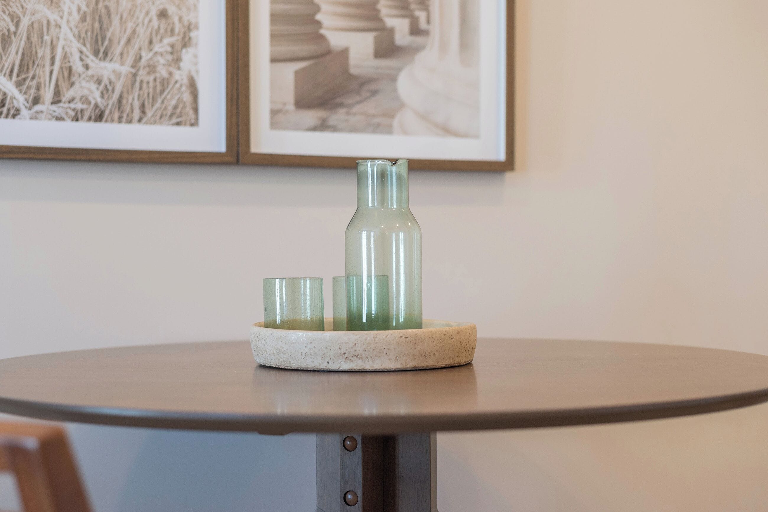 Una mesa redonda con una jarra de vidrio y dos vasos sobre un posavasos de piedra.