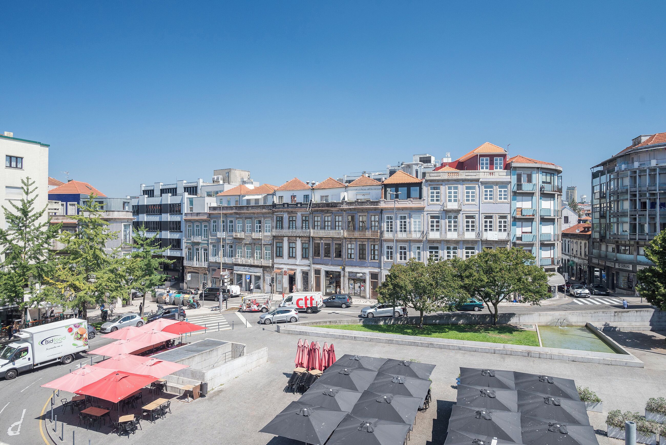 A row of multi-story buildings with a central courtyard, outdoor seating, and a visible food delivery service.