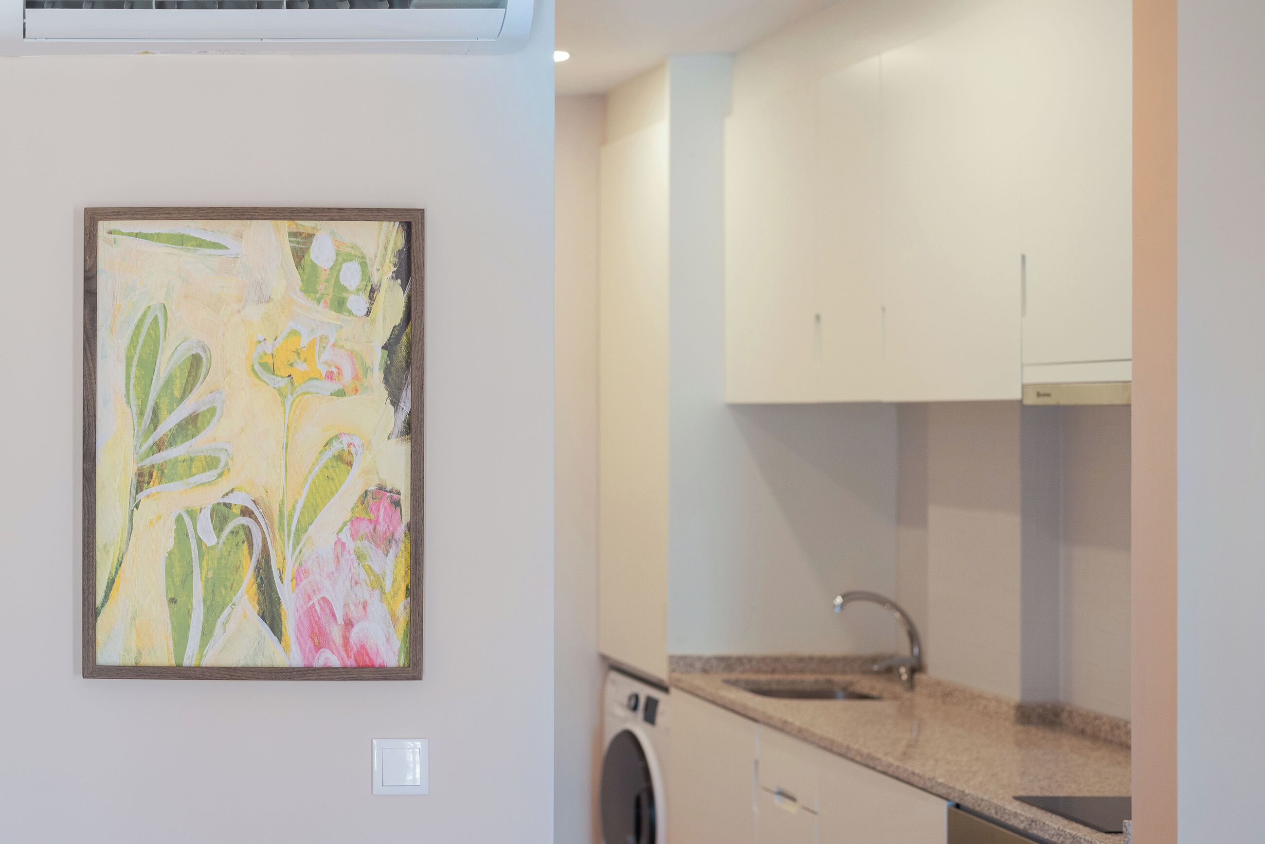 A kitchen with a washing machine, a sink, and a framed abstract painting on the wall.
