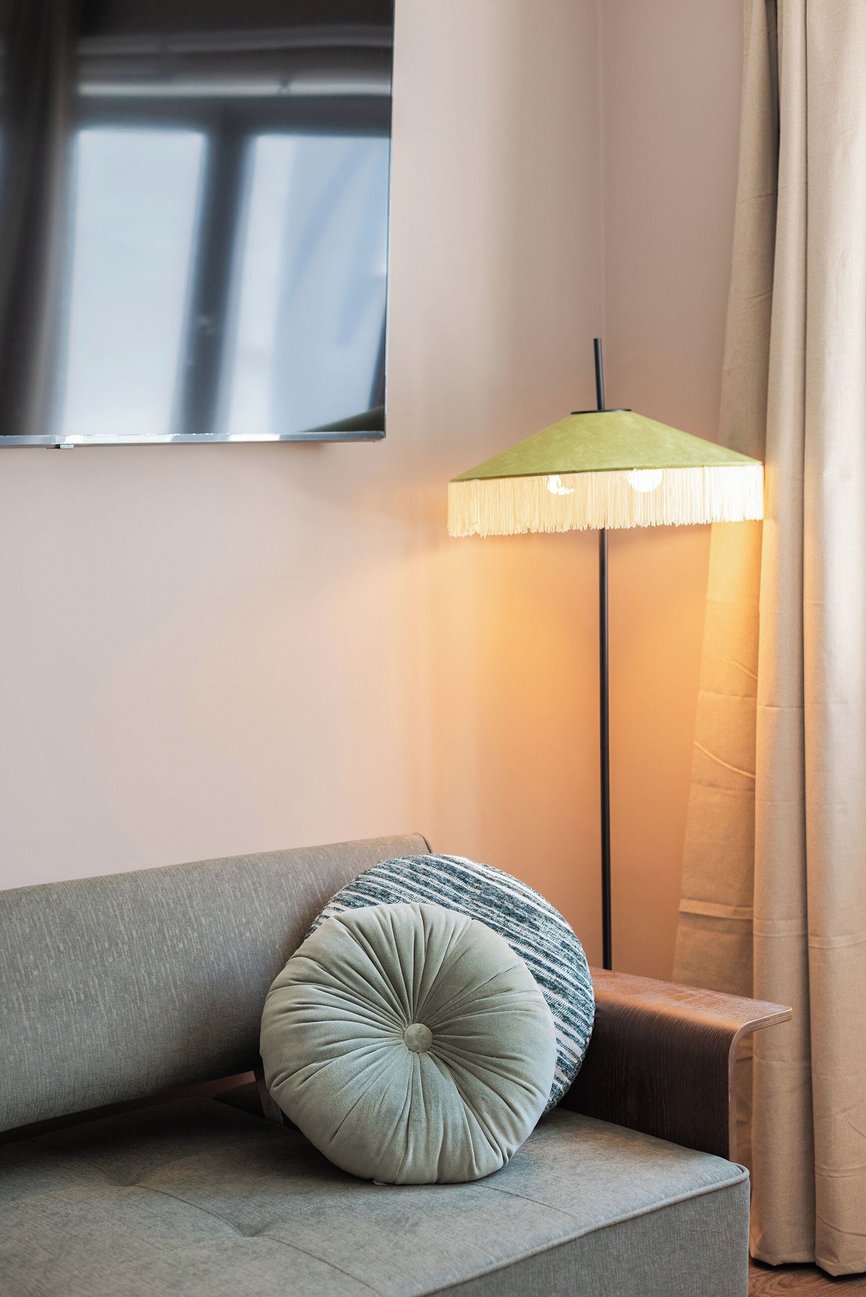 Una habitación con sofá, una lámpara de pie verde y una ventana con cortinas.