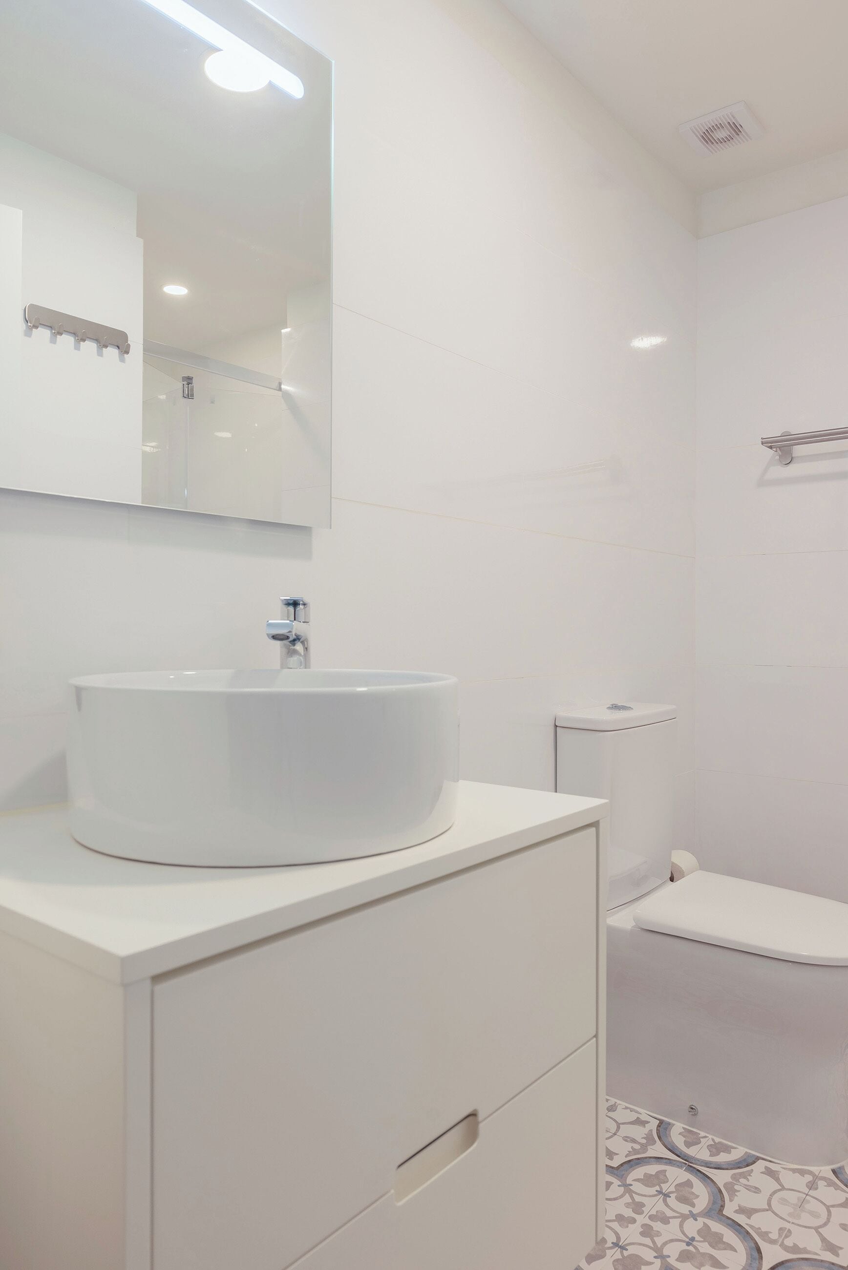 A modern bathroom with a white sink, mirror, and toilet.