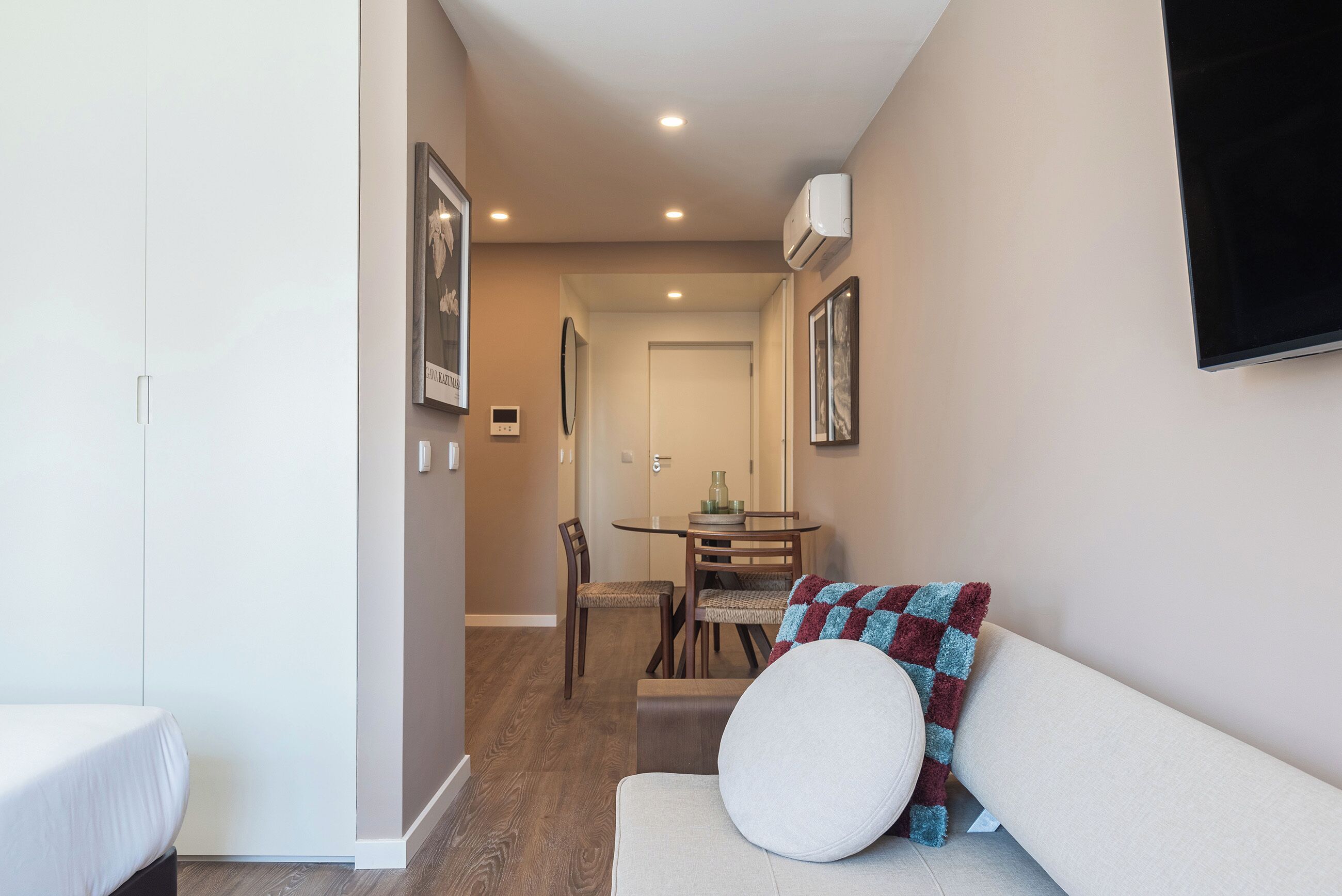 Una sala de estar moderna con un sofá, una mesa de comedor con sillas y un pasillo que lleva a una puerta.