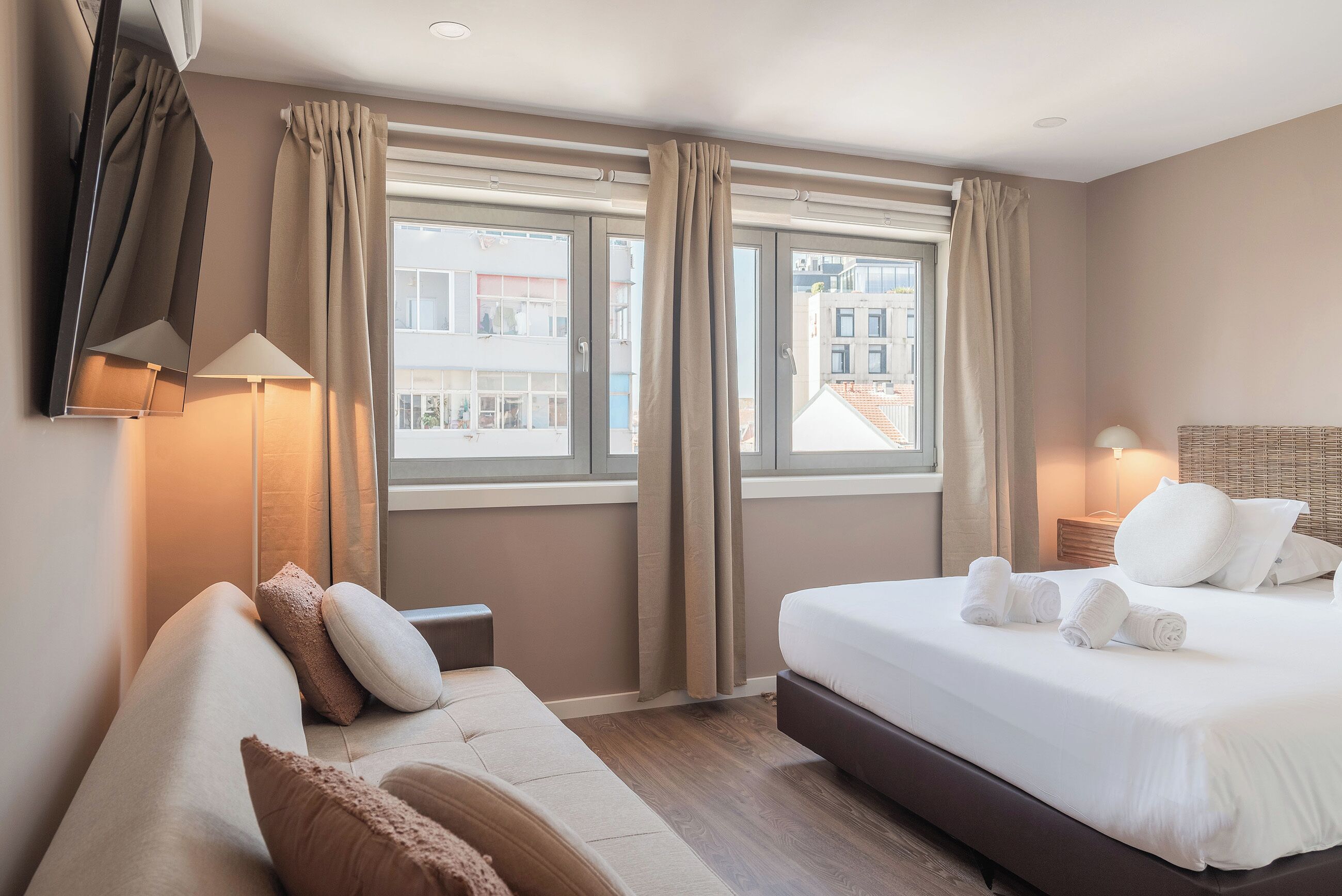 Habitación de hotel con cama, sofá, televisor y ventana con cortinas.