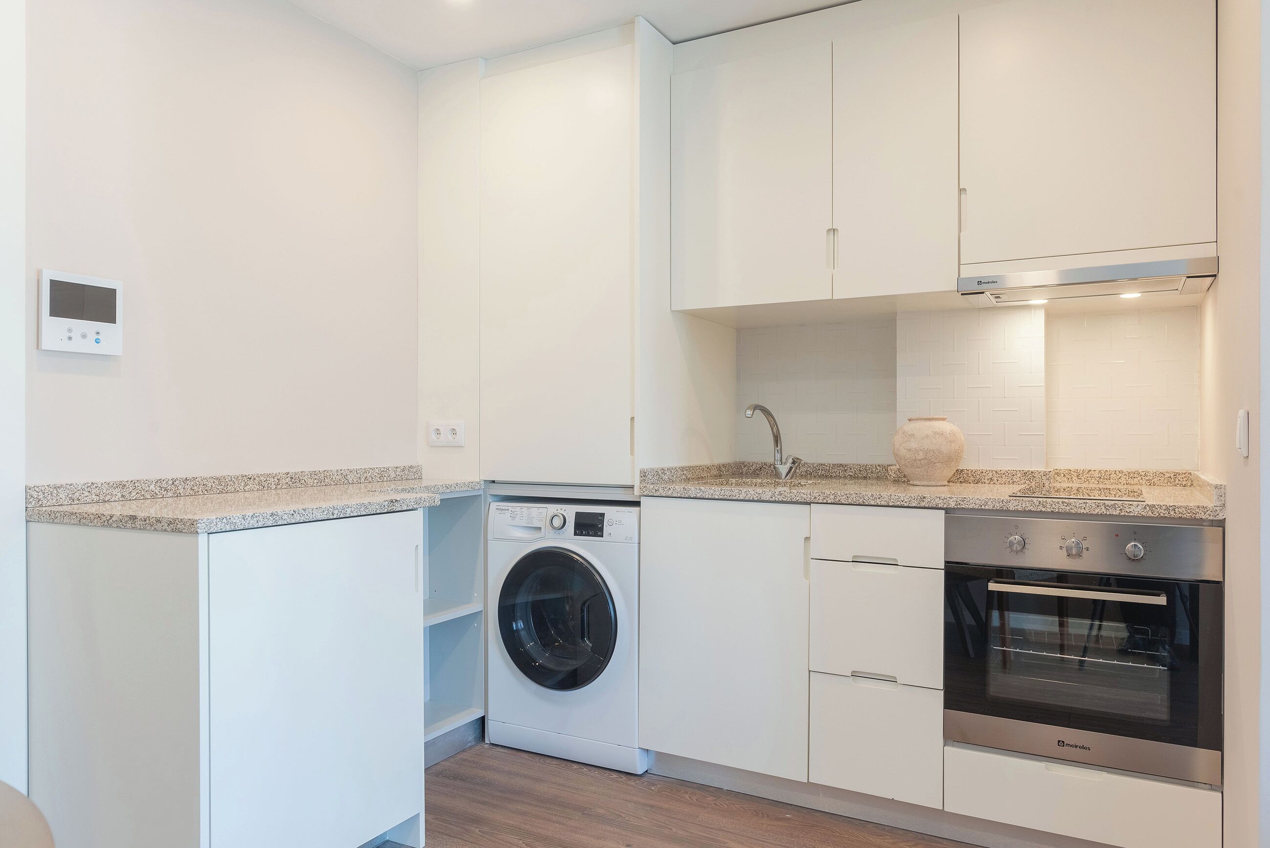 Une cuisine compacte équipée d’un lave-linge, d’un four et d’un plan de travail en granit.