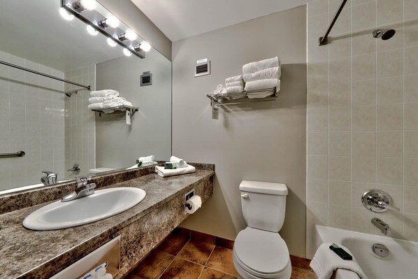 A modern bathroom with a double sink, toilet, and bathtub. There are towels and toiletries on the counter.