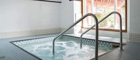 Ein Schwimmbecken mit Metallleitern, Fliesenboden und einem Fenster mit Blick auf Grünflächen.