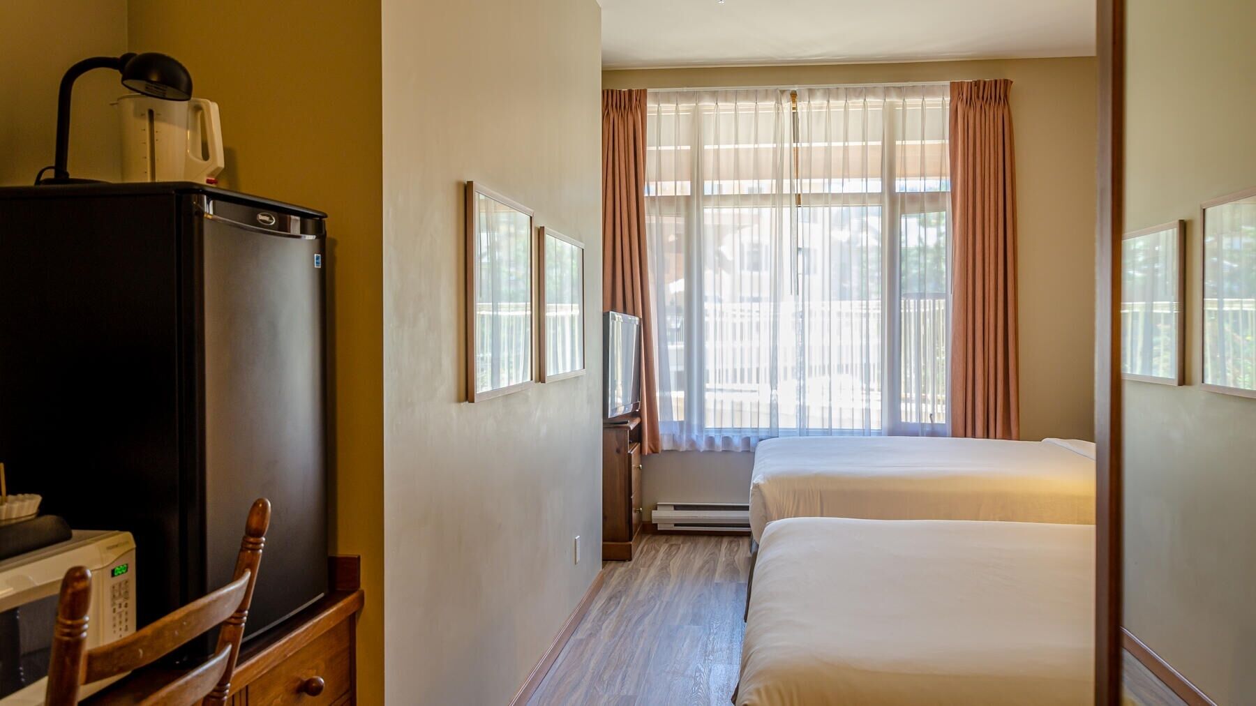 Habitación de hotel con cama, escritorio con computadora, refrigerador y ventana con cortinas.