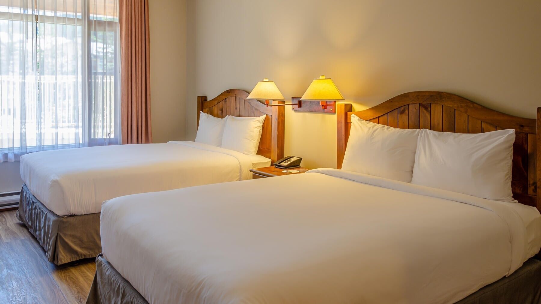 A hotel room with two beds, wooden headboards, and bedside lamps.