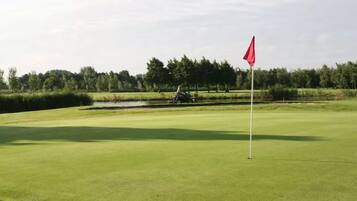 A golf course with a flag, a pond, and a tractor in the background.