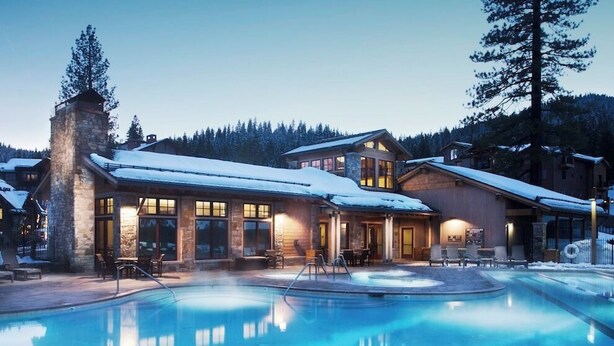 Een lodge met zwembad, stenen gevel en grote ramen.