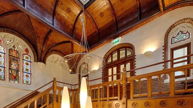 A grand wooden staircase with intricate designs and multiple levels, leading to a high ceiling with a skylight.
