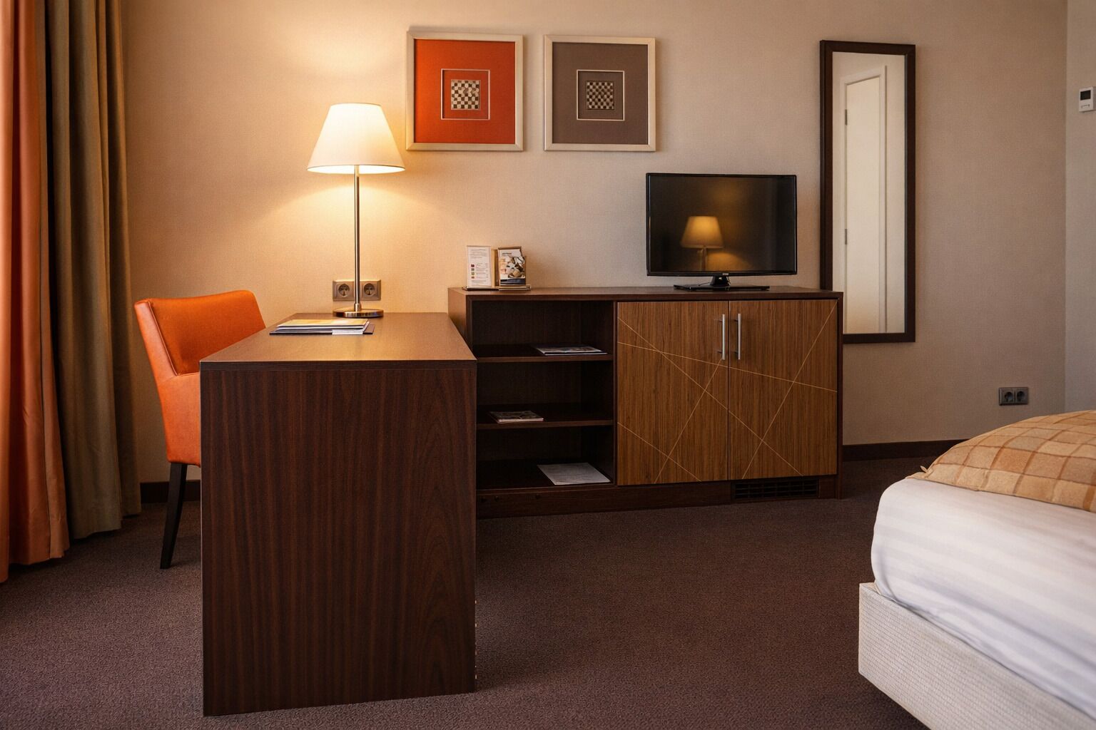 A hotel room with a desk, chair, TV, and bed.