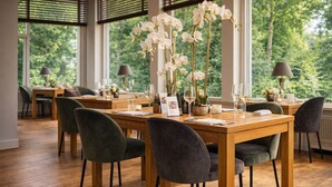 A dining area with wooden tables, dark chairs, and a vase of white orchids. - Peaceful Nature Stay Just Minutes from Lively Groningen Attractions! Pool! (Paterswolde)