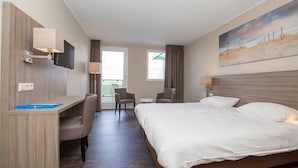 A hotel room with a bed, desk, chairs, and a TV. - Sun, Sand & Swings | Soothing Escape w/ Golf, Pool & Beach Minutes Away (Callantsoog)