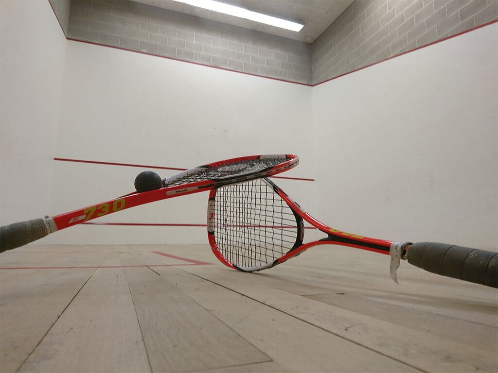 Un court de squash avec une raquette rouge et noire, une balle de squash et un filet.