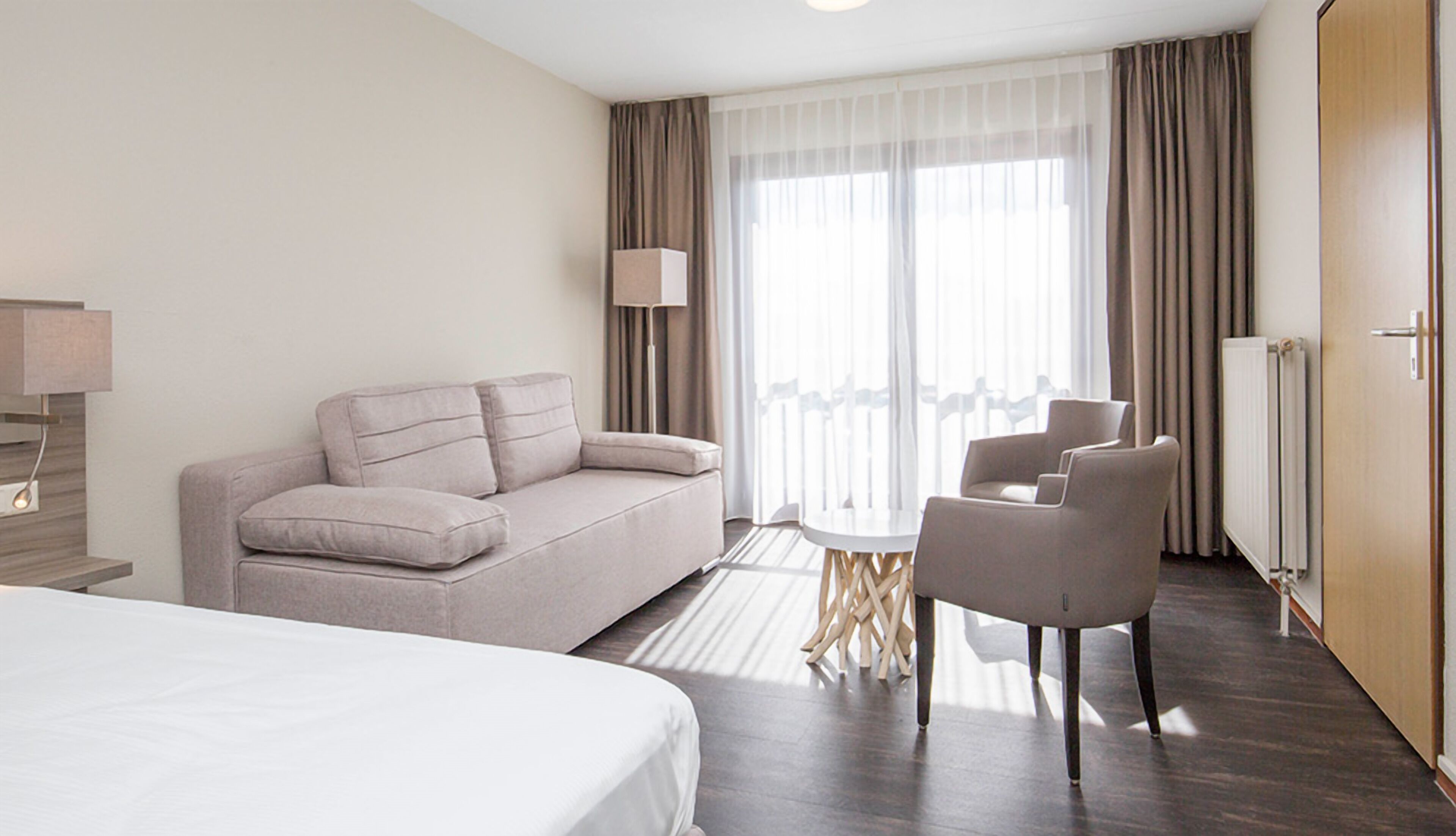 Une chambre d’hôtel avec un lit, un canapé, une chaise, une table et une fenêtre avec des rideaux.