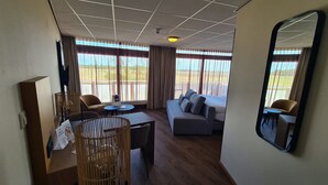 A hotel room with a large window, a sofa, a dining table, and a mirror. - Relaxing Haamstede Haven | beach escape, Scenic Nature trails, Local attractions (Burgh-Haamstede)