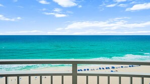 Une vue sur la plage, avec un ciel dégagé, une mer turquoise et un balcon agrémenté de parasols bleus.